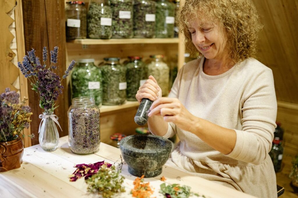 Erborista che macina erbe con mortaio e pestello tra barattoli e fiori secchi